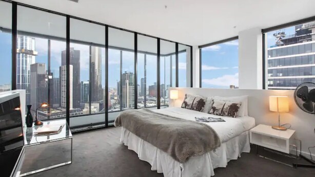 Una habitación de hotel moderna con una cama grande, un escritorio de vidrio y vistas a la ciudad.