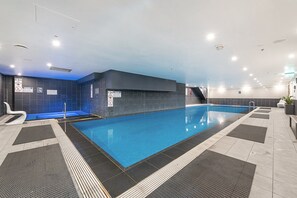An indoor swimming pool with clear safety signage, a diving board, and a modern design with tiled walls and a ceiling with recessed lighting. - Incredible City Views in Convenient CBD Apartment (Melbourne)