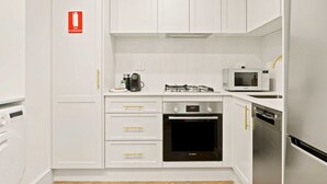 A compact kitchen with white cabinets, a Bosch oven, a microwave, and a dishwasher. - City Centre Studio by Hyde Park (Sydney)