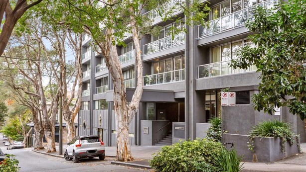 A modern multi-story building with balconies, a car parked on the street, and trees lining the sidewalk. - City Centre Studio by Hyde Park (Sydney)