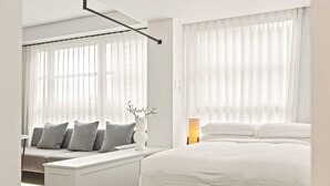 A modern hotel room with a bed, a seating area with cushions, and large windows with sheer curtains. - City Centre Studio by Hyde Park (Sydney)