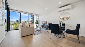 A modern living room with a sofa, dining table, and chairs. There is a large window offering a city view. - Chic 1-bed With Sophisticated Decor, (Canberra)