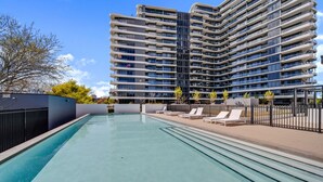 A modern hotel with a rooftop pool, lounge chairs, and a high-rise building in the background. - Chic 1-bed With Sophisticated Decor, (Canberra)