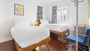 A room with two beds, a ceiling fan, a window with curtains, a bedside table with a lamp, and a chair.