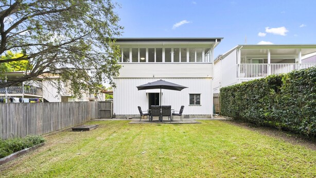 A two-story house with a covered patio area, a fenced backyard, and a well-maintained lawn.