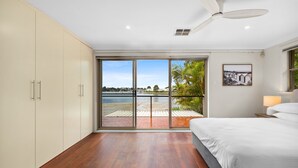 A bedroom with a large sliding glass door leading to a balcony with a view of a body of water and greenery. - Modern 3-bed With Pool & Water Views by Beach (Sydney)