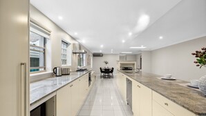 A modern kitchen with a long countertop, built-in oven, and a dining area with a table and chairs. - Modern 3-bed With Pool & Water Views by Beach (Sydney)