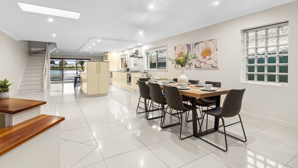 A modern kitchen with a dining area, featuring a staircase leading to an upper level, a large window with a view, and a clean, tiled floor. - Modern 3-bed With Pool & Water Views by Beach (Sydney)