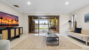 A spacious living room with a large window, a flat-screen TV, a sofa, and a coffee table. - Modern 3-bed With Pool & Water Views by Beach (Sydney)