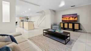 A modern living room with a sofa, coffee table, and a painting of a sunset. - Modern 3-bed With Pool & Water Views by Beach (Sydney)