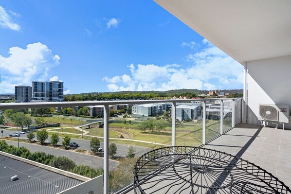 A balcony with a clear view of a modern building complex, a road, and greenery.