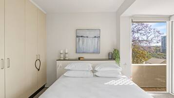 Una camera da letto con un letto, un comodino, un quadro e vista su un balcone alberato.