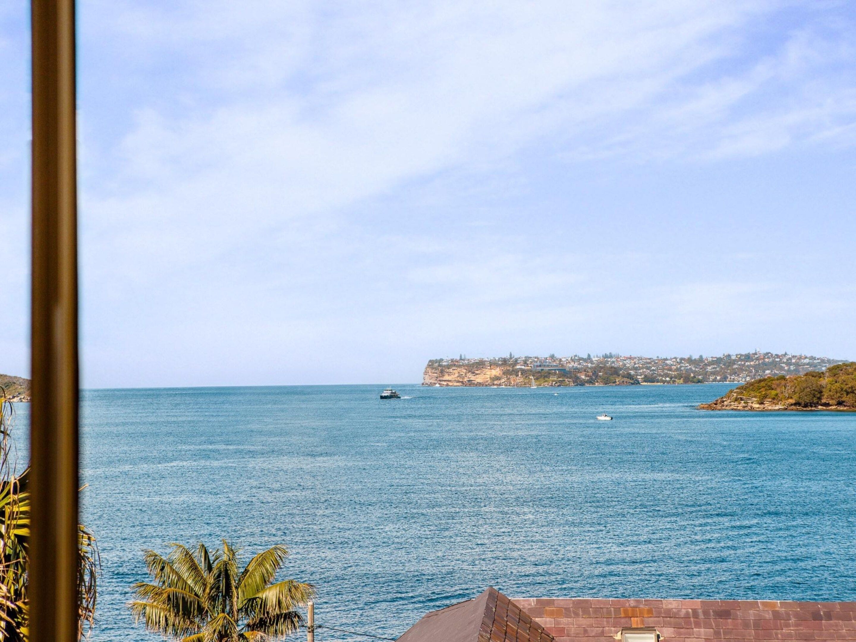 Vista sulla costa con cielo sereno, mare calmo e una linea di costa lontana con edifici.