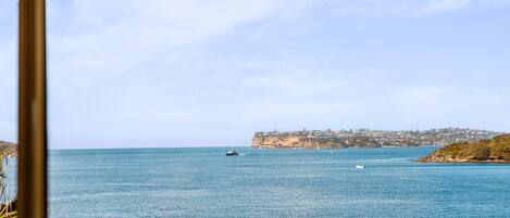 Vista sulla costa con cielo sereno, mare calmo e una linea di costa lontana con edifici.