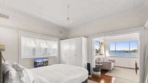 Ein Schlafzimmer mit einem großen Bett, einem Fernseher, einem Schreibtisch und Blick auf das Meer.