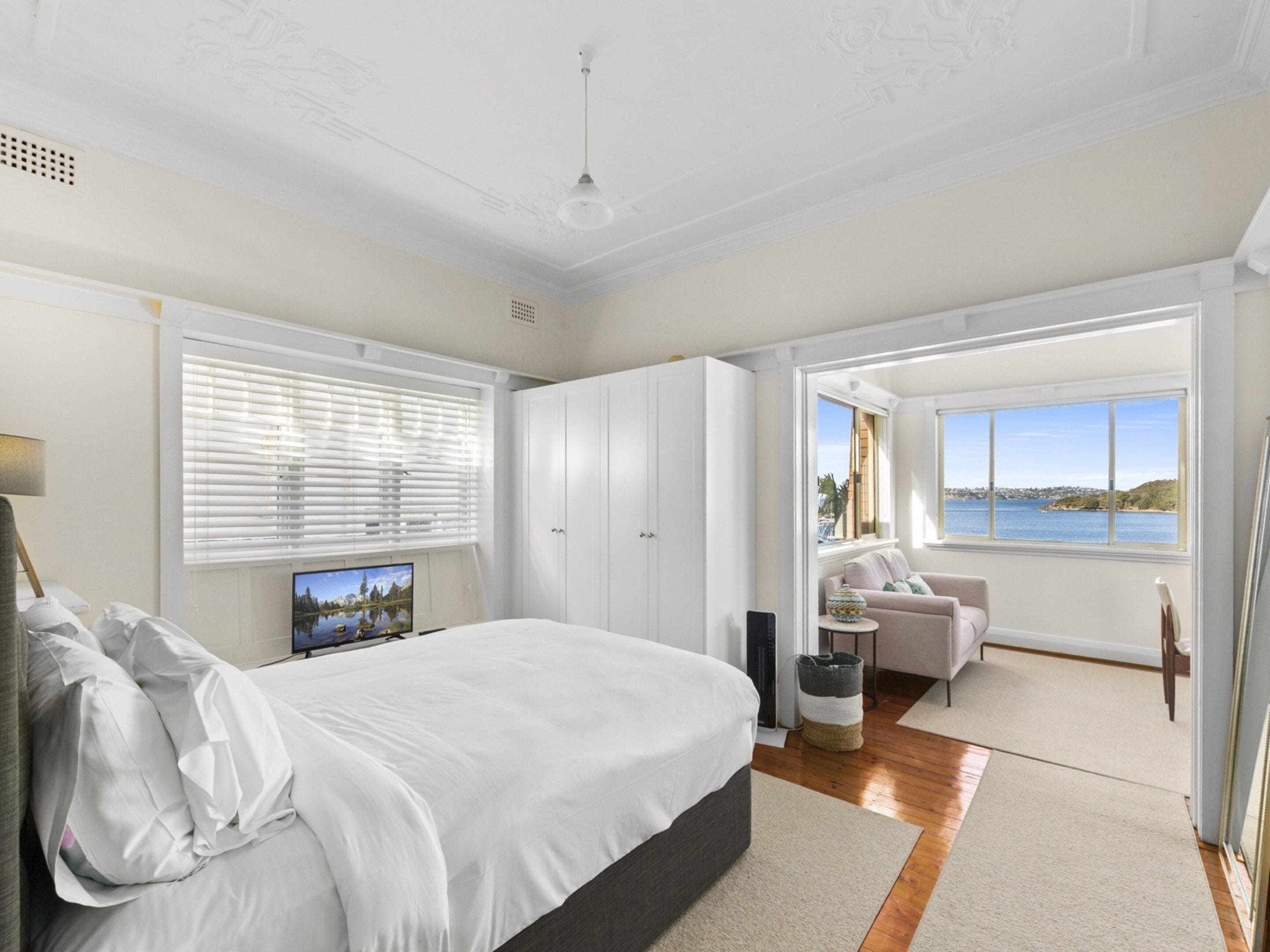 Un dormitorio con cama, televisor, ventana con persianas, sofá y vista a un cuerpo de agua.