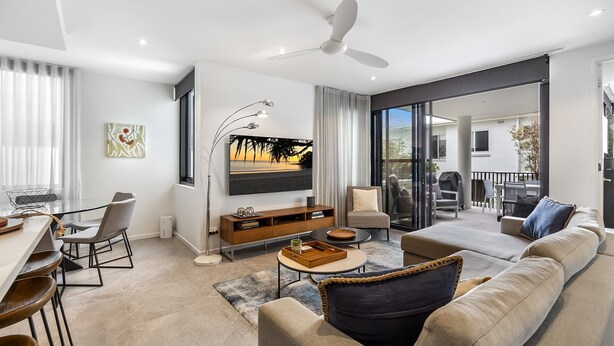 A modern living room with a sofa, dining area, and a large TV.