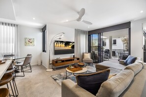 A modern living room with a sofa, dining area, and a large TV. - Coastal Bliss: 3-bedroom Retreat With Pool (Sunshine Coast)