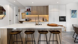 A modern kitchen with a central island, bar stools, and a microwave.