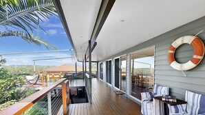 Une vaste terrasse avec un plancher en bois, une bouée de sauvetage fixée au mur et des sièges d’extérieur dotés de coussins à rayures.