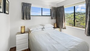 Une chambre à coucher avec un grand lit, des murs blancs et une fenêtre avec des rideaux.