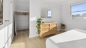 Ein Schlafzimmer mit Bett, Kommode, Spiegel und Fenster.