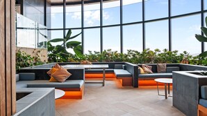 A modern indoor seating area with high ceilings and large windows, featuring multiple seating options and a central table.