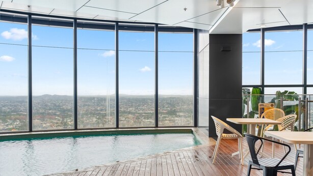 A spacious indoor area with a large window overlooking a cityscape, a wooden floor, and a table with chairs.