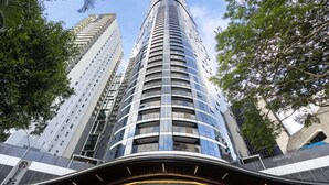 A modern high-rise building with a curved facade, surrounded by trees and other tall structures.