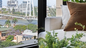 A modern living room with a large window overlooking a cityscape, including a cable-stayed bridge and buildings.