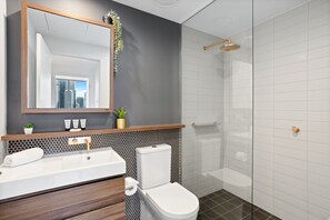 Un baño moderno con un espejo grande, un lavabo, un inodoro y una ducha.