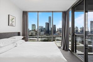 Habitación de hotel con una cama grande, vistas de la ciudad a través de ventanas del suelo al techo, y una obra de arte con forma de piña en la pared.