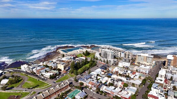 An aerial view of a coastal town with a beachfront, residential buildings, and a large hotel with multiple floors. - Charming Townhouse Steps From Newcastle Beach (Newcastle)