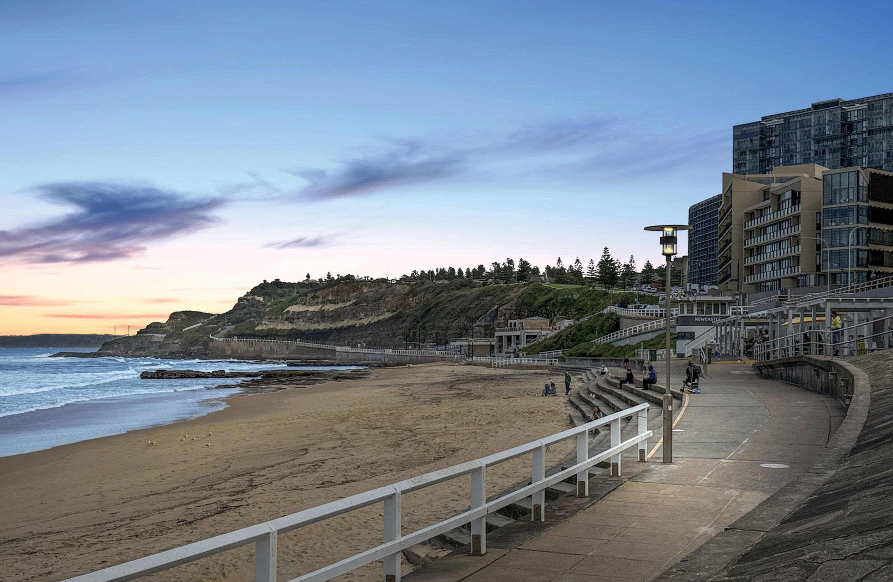 A coastal walkway leading to a beach with a view of cliffs and buildings.