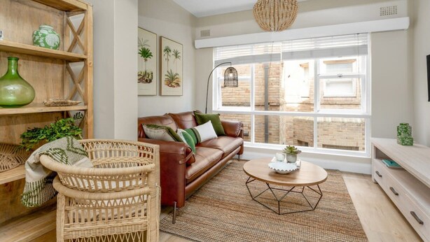 A modern living room with a leather sofa, wicker chairs, a round coffee table, and a large window with a view of brick buildings. - Spacious 2-bed Apartment in the Heart of Manly (Sydney)