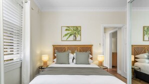 A hotel room with a large bed, two bedside lamps, a wooden headboard, and a framed picture of a palm tree on the wall. - Spacious 2-bed Apartment in the Heart of Manly (Sydney)