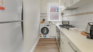 A compact kitchen with a refrigerator, washing machine, stove, and cabinets. - Spacious 2-bed Apartment in the Heart of Manly (Sydney)