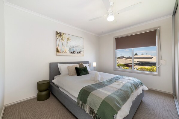 A neatly made bed with a green and white checkered blanket, a grey headboard, and a wall-mounted painting of a van and palm trees. - Large Upstairs Family Stay Near Middleton Beaches (Middleton)