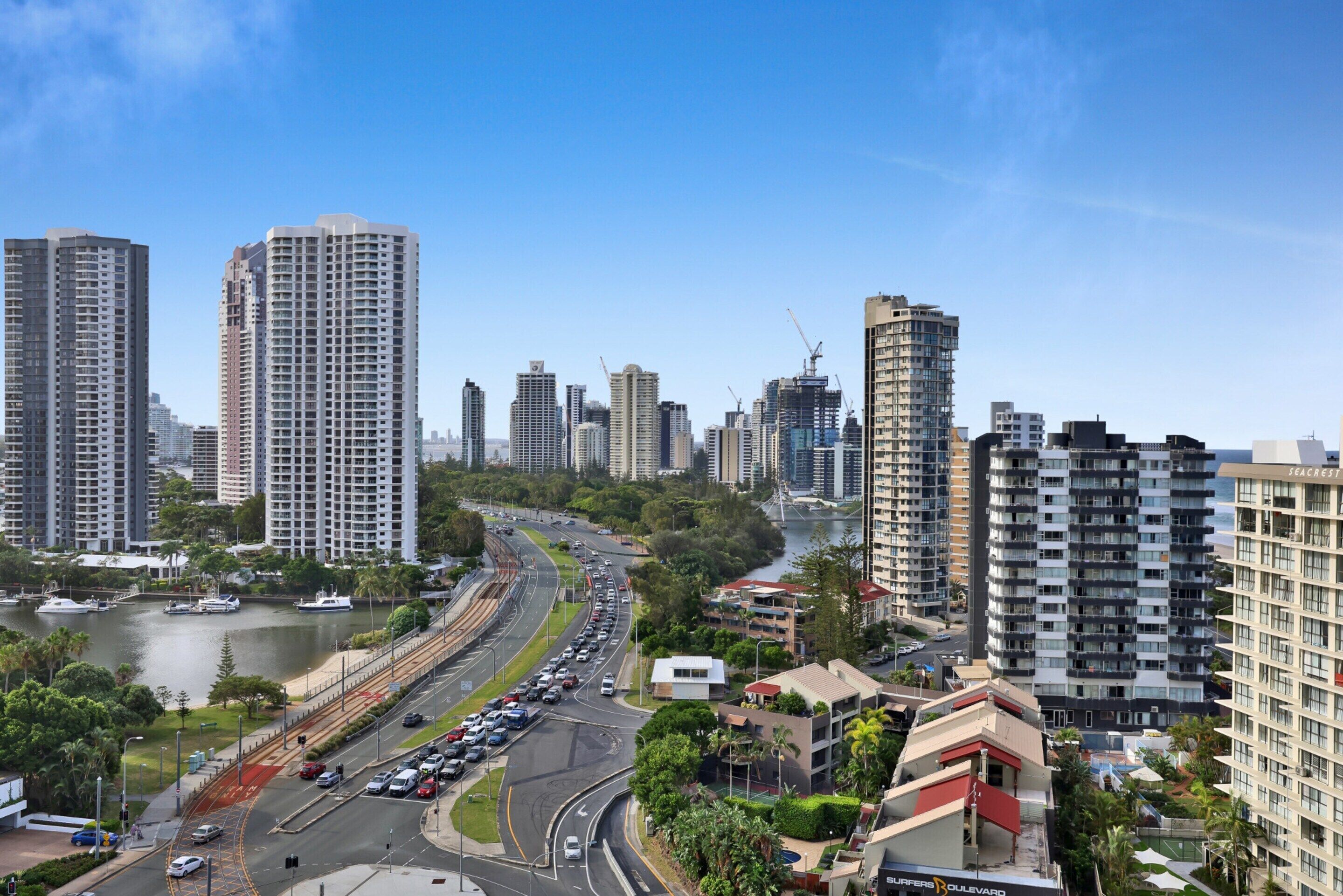 A high-rise building with multiple floors and balconies, surrounded by other high-rise buildings and a body of water.