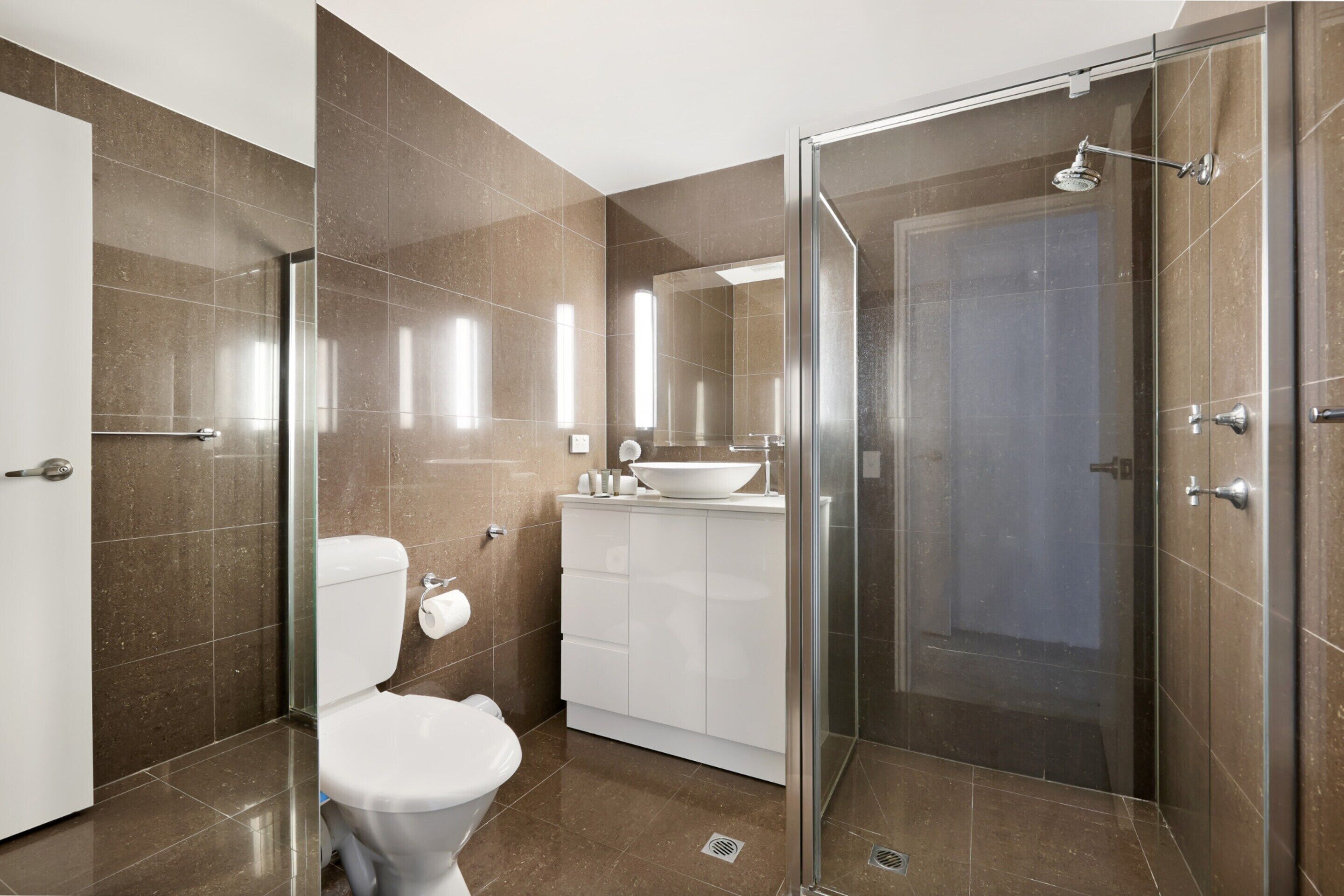 A modern bathroom with a glass shower enclosure, a white toilet, and a vanity with a sink.