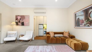Ein Wohnzimmer mit einem braunen Sofa, zwei weißen Sesseln, einem rosa Teppich und einem Bild an der Wand.