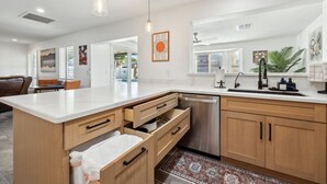 Uma cozinha moderna com ilha central, armários de madeira, lava-louças e iluminação pendente.