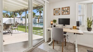 Um escritório moderno com uma mesa grande, computador e vista para um quintal com piscina.