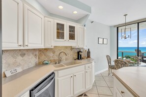 A kitchen with white cabinets, a stainless steel dishwasher, and a view of the ocean through a large window.