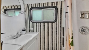 A compact bathroom with a white sink, a mirror, a window, and striped wallpaper.
