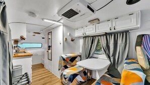 A compact RV interior with a kitchenette, a small dining area, and a sleeping berth.