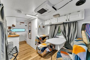 A compact RV interior with a kitchenette, a small dining area, and a sleeping berth.