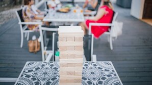 A wooden block tower on a table with a patterned tablecloth, set on a deck with outdoor seating.