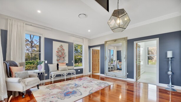 A spacious living room with a large rug, a sofa, and a coffee table. There is a large mirror on the wall and a window with curtains.