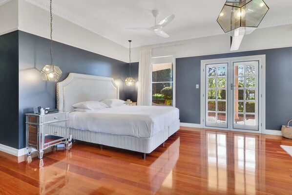 A bedroom with a large bed, a nightstand, a ceiling fan, and a view of the outdoors through a glass door.